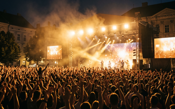 Koncert na otvorenom tokom Rumskog kulturnog leta — publika ispred bine na gradskom trgu uveče